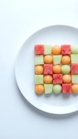 Colorful fruit salad arranged in geometric pattern on white plate featuring watermelon, cantaloupe and honeydew melon cubes for healthy eating concepts.