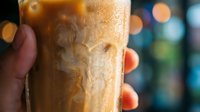 Iced coffee drink held in hand with blurred city lights in background, refreshing beverage for cafes, restaurants, summer menus, and beverage marketing campaigns.