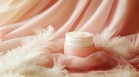 Luxurious face cream jar on soft pink silk fabric with delicate white feathers creating elegant cosmetic product composition for beauty and skincare advertising.