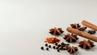 Aromatic winter spices including cinnamon sticks, star anise, cloves and chili flakes arranged on neutral background for seasonal cooking and baking.