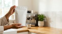 Woman holding white stand-up pouch packaging in kitchen, displaying product mockup for food, supplements, or retail goods packaging design.