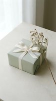 Sage green gift box tied with a cream ribbon bow, styled with dried wildflowers on a neutral surface in soft natural light.