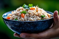 Steamed rice with diced carrots and fresh herbs served in blue ceramic bowl against blurred green background, close up view of homemade Asian cuisine.