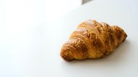 Fresh golden croissant with flaky layers on clean white background, perfect for bakery menus, food blogs, breakfast concepts and culinary designs.