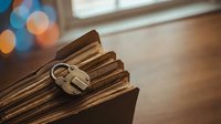 Vintage brass padlock securing stack of old leather-bound books on wooden surface with warm bokeh lights creating cozy atmosphere for security concepts.