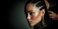 Young African American woman with braided hairstyle and dramatic makeup wearing statement earrings against dark background for beauty and fashion concepts.