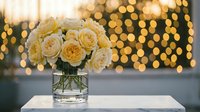 Elegant cream roses in glass vase with warm golden bokeh lights creating romantic atmosphere for wedding celebrations and special occasions.