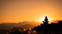 Young woman practicing yoga meditation pose on mountain peak during golden sunset with layered hills silhouette for wellness and mindfulness concepts.