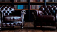 Luxurious brown leather chesterfield armchairs with classic button tufting and rolled arms against library bookshelf background, elegant vintage furniture design.