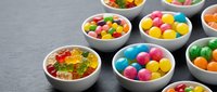 Colorful assorted candies and sweets in white bowls on dark slate background for confectionery business, party planning and dessert displays.