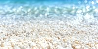 Soft focus macro view of white coral sand with turquoise ocean water and sparkling bokeh effect in background, tropical beach shoreline nature scene.