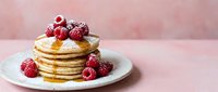 Stack of golden pancakes topped with fresh raspberries and powdered sugar on white plate against soft pink background for breakfast menu design.