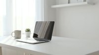 Laptop with coffee mug and succulent plant on white desk near window in bright, minimalist home office workspace.