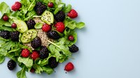 Fresh green salad with mixed berries, cucumber slices and chia seeds on light blue background. Healthy eating concept with copy space for text.