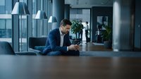 Professional businessman in blue suit using smartphone in modern office lobby with contemporary lighting and urban architecture for corporate communications.