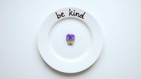 Be kind text on white ceramic plate with purple pansy flower, minimalist kindness concept for mental health and positivity.