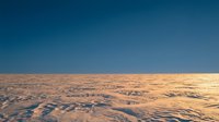 Aerial view of vast desert landscape with undulating sand dunes and shadows creating natural patterns under clear blue sky, suitable for travel and nature backgrounds.