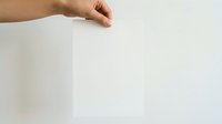 Hand holding blank white paper sheet against neutral background, suitable for mockups, presentations, and advertising campaigns.