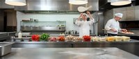Professional chefs working in modern commercial restaurant kitchen with stainless steel equipment and fresh ingredients for culinary food preparation.