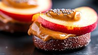 Fresh red apple slices layered with creamy caramel and chocolate on dark brownie base, topped with sprinkles, macro food photography on black background.