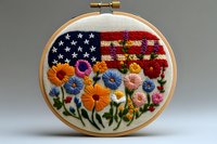 Embroidered American flag with colorful flowers in wooden hoop. Patriotic needlework art combining stars and stripes with floral garden design for crafting.