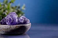 Purple amethyst crystals in ceramic bowl with green plant background for wellness meditation and spiritual healing practices.