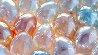 Luminous freshwater pearls in soft pastel colors showing natural iridescence and organic shapes, arranged in elegant cluster formation with delicate light reflections.