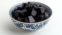 Black grass jelly dessert cubes in traditional blue and white porcelain Chinese bowl with floral pattern, cooling Asian sweet delicacy on white background.