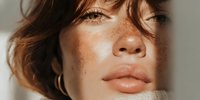 Young woman with freckles and natural makeup in soft lighting. Portrait of caucasian female with brown hair and golden earrings for beauty and skincare concepts.