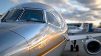 Close-up of private jet nose and cockpit at airport during sunset with dramatic sky and another aircraft in background.