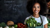 Young African American woman in white t-shirt holding fresh organic produce and vegetables at farmers market or local grocery store, displaying healthy food with genuine smile.