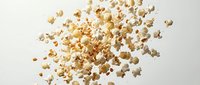 Scattered popcorn kernels floating in air against clean white background, perfect for food advertising and snack marketing campaigns.