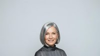 Mature woman with gray hair and fair complexion wearing dark turtleneck against neutral background, suitable for corporate, healthcare, and lifestyle editorial use.