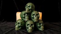 Stacked green textured skulls with glowing candle behind on dark surface, suitable for Halloween, gothic, and spooky themed designs.