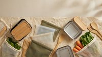 Flat lay arrangement of eco-friendly kitchen items including wooden utensils, glass containers, and fresh vegetables on natural linen fabric for sustainable lifestyle and zero-waste cooking content.