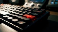 Close-up of modern gaming keyboard with illuminated keys and red accent lighting on dark surface for technology and gaming setup concepts.