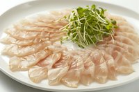Fresh raw fish sashimi slices arranged on white plate with green microgreens garnish for Japanese cuisine and seafood dining experiences.