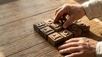 Senior businessman hands arranging wooden blocks with business icons on rustic table, strategic planning and corporate decision making concept.