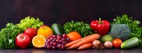 Fresh organic produce panorama with colorful fruits and vegetables arranged on dark background, including tomatoes, citrus, grapes, carrots and leafy greens.
