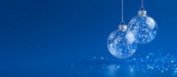 Transparent glass Christmas ornaments with snowflake pattern hanging against deep blue background with bokeh lights for holiday designs.
