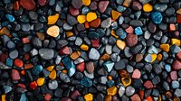 Colorful decorative stones background with vibrant orange, blue, red, and yellow pebbles mixed with dark gray rocks creating textural contrast for landscaping or garden design.