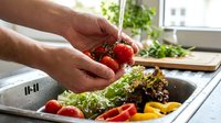 Male hands washing fresh red tomatoes in kitchen sink with mixed salad vegetables for healthy meal preparation and cooking at home.