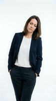 Middle-aged woman with long dark hair and fair complexion wearing navy blazer and white top, hands in pockets, looking down thoughtfully against white background for corporate and business use.