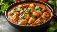 Juicy meatballs in rich tomato sauce garnished with fresh basil leaves served in rustic ceramic bowl on concrete background, homestyle comfort food.