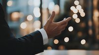 Close-up of businessman's hand gesturing against blurred bokeh lights background, creating atmosphere of professional communication in evening urban setting.