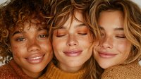 Three diverse young women with natural freckled skin embracing in warm golden light, showcasing friendship, beauty and sisterhood in earth tone clothing.
