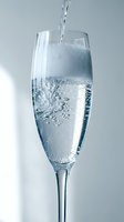 Clear sparkling water being poured into elegant champagne flute glass with bubbles and foam against neutral background for beverage concepts.