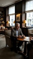 Mature male professional with gray hair, Caucasian ethnicity, wearing business casual attire, seated in upscale office lounge during meeting or consultation with colleague.