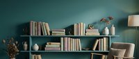 Modern home library interior with floating shelves displaying books and decorative vases against teal wall. Cozy reading corner with armchair and lamp.