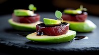 Fresh avocado slices topped with tuna sashimi, dark soy sauce drizzle, and lime garnish on black slate plate, elegant appetizer presentation for fine dining.